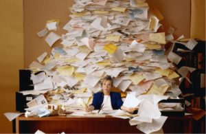 Picture of an office space filled with paper, unable to complete tasks because of the confusion.